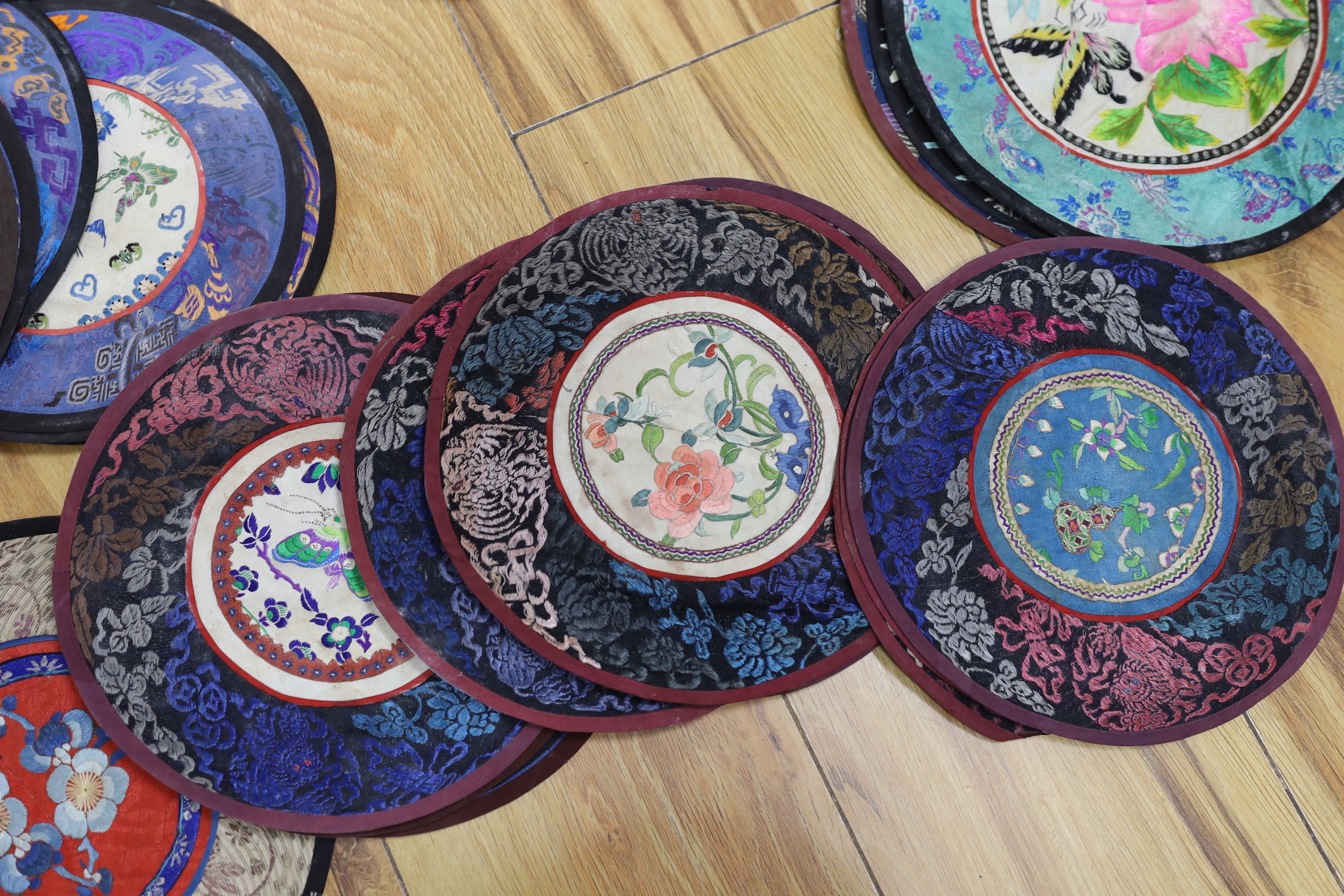 Forty two Chinese embroidered circular mats with damask borders, largest 25cm in diameter